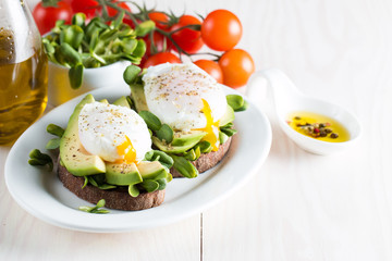 Avocado toast, cherry tomato on wooden background. Breakfast with toast avocado, vegetarian food, healthy diet concept. Healthy sandwich with avocado and poached eggs.