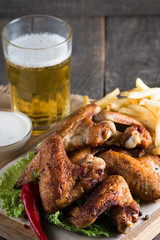 Close-up photo of bbq chicken wings with fries and beer. Barbeques meat with sauces, ketchup, mayonnaise. Fast and junk food concept. 