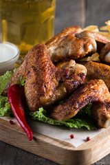 Close-up photo of bbq chicken wings with fries and beer. Barbeques meat with sauces, ketchup, mayonnaise. Fast and junk food concept. 
