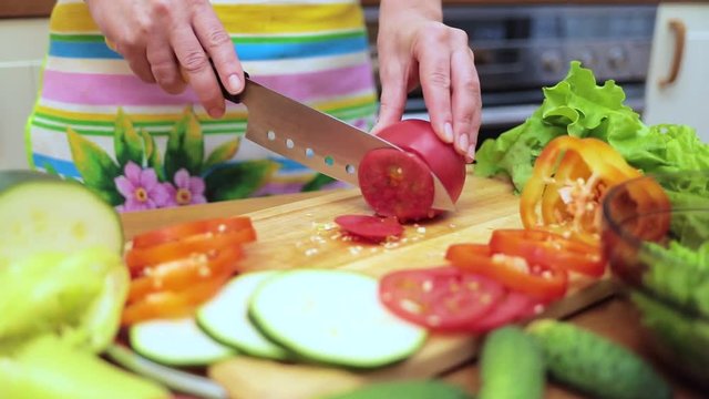 Women's hands Housewives cut with a knife fresh tomato on the cutting Board of the kitchen table