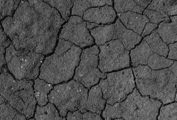 Black cracked surface of grey soil texture background, dark dried and chopped gray earth, old fissure dark ground, close-up, erosion