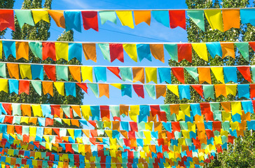 Multicolored flags a triangular shape  against the blue sky and trees. Good background on the theme of a city street holiday