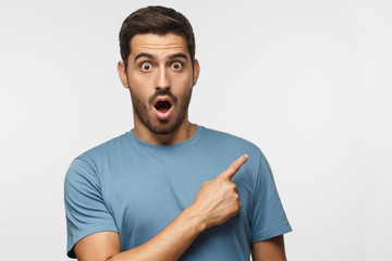Young surprised man isolated on gray background in blue t-shirt looking at camera with open mouth,...