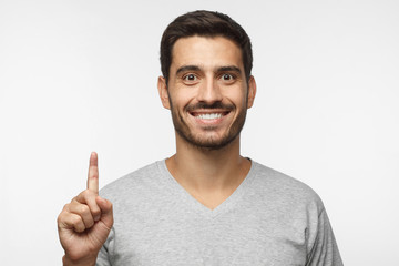 Attractive young man pointing up with his finger isolated on gray background