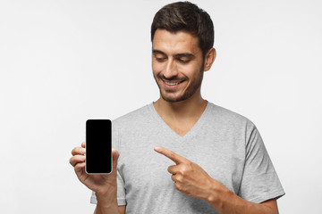Portrait of happy man demonstrating blank smartphone and pointing to empty blank screen with smile. Copyspace for yor app