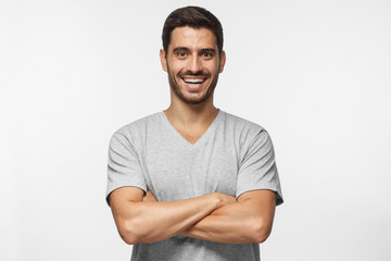 Portrait of laughing handsome man in blue t-shirt standing with crossed arms isolated on grey...