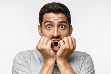 Young man covering mouth with hands and round eyes, experiencing deep astonishment and fear,...