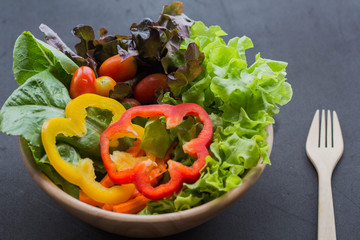 Bowl of fresh vegetable salad with wooden fork on black background.Clean eating, dieting, vegan food concept.