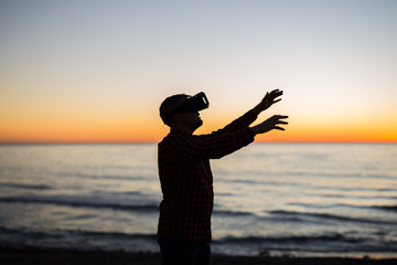 Fototapeta premium Young man using virtual reality glasses on over beautiful sky background