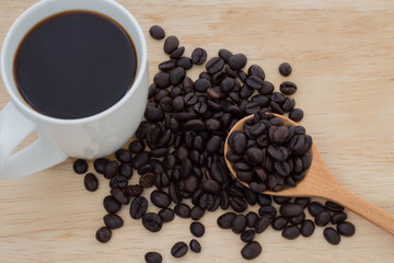 Coffee beans in wooden spoon with white cup on wood table. Coffee is a popular drink and is known around the world.