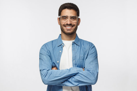 Portrait of smiling handsome man in blue shirt standing with crossed arms isolated on gray background