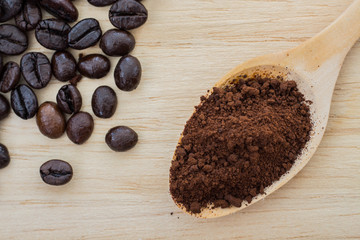 coffee beans and powder coffee in spoon on a wooden background.