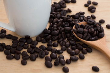 Close-up Coffee beans in wooden spoon with white cup on wood table. Coffee is a popular drink and is known around the world.