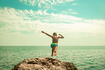 A boy is jumping from the cliff into the sea on a hot summer day. Holidays on the beach. The...