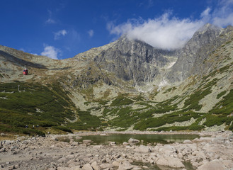 Fototapeta na wymiar View on mountain Peak Lomnicky stit 2 634 m covered in clouds at Summer, in the High Tatras mountains of Slovakia with mountain lake Skalnate pleso and red cable car cabine, Vysoke Tatry
