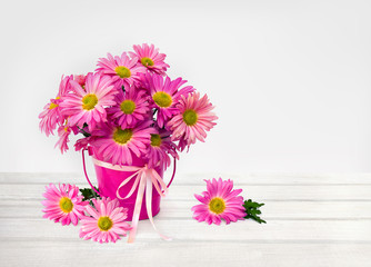 Bouquet of flowers pink chrysanthemum daisies in small decorative pink bucket with ribbon on white wooden table on a light background with space for text