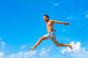 Fototapeta na wymiar young man doing parkour jump on the blue sky background on sunny summer day