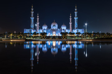 Fototapeta na wymiar Grand Mosque in Abu Dhabi at night in the United Arab Emirates (UAE) in a Reflective Pond looking at the glowing Islamic iconic symbol. Ramadan call to prayer.