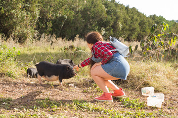 Happy young woman plays with little wild boars on nature.
