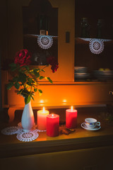 View of an old vintage painted cupboard with with lit candles in a dark room, with old dishes, roses in a vase, and leaves,  in a dark room. Autumn composition or hello autumn background. 