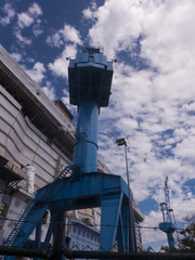 Ein blauer Kran ragt in den wolkigen Himmel.
Baukran, 