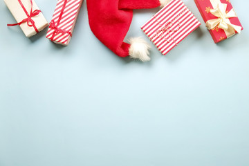 Santa Claus hat & new year presents wrapped in festive colorful craft paper and silk bow arranged in festive composition. Close up background, copy space, top view. Winter holidays preparation concept