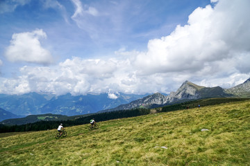 Fototapeta premium Zwei Mountainbiker über Wiese mit Panoramablick in die Berge