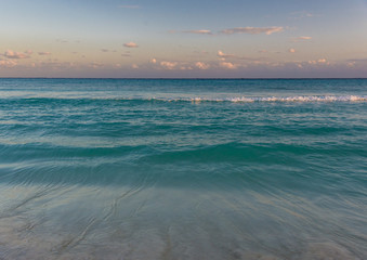 The tropical blue waters of the Caribbean Sea lap at the beach in Cancun, Mexico, as the day ends.