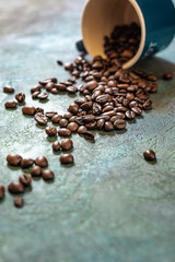 Roasted coffee beans with small cup, scattered on rustic blue and green table 