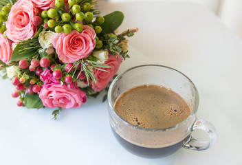 black coffee in a glass transparent mug next to a bouquet of flowers, pink roses