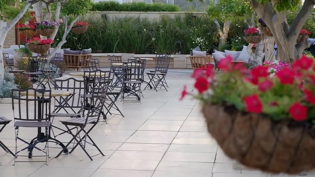Conducting of the camera at the left on the right and refocusing from little tables in a garden on a suspended pot with flowers