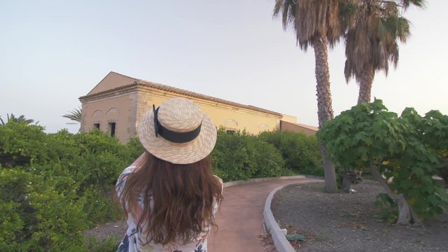 Beautiful woman making mobile photo of nice luxury villa. Young girl taking photo of old hotel territory . Dressed in white dress and hat. Female tourist.Elegant girl have good moments