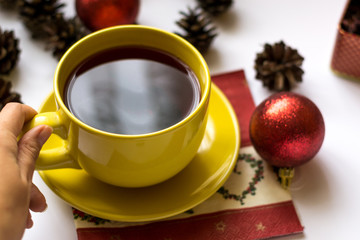 New year and christmas composition of yellow cup of hibiscus tea in hand, Christmas tree cones, tea box and red decorations isolated on white background.
