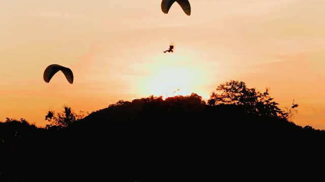 silhouette flying paramotor over mountain and sunset sky