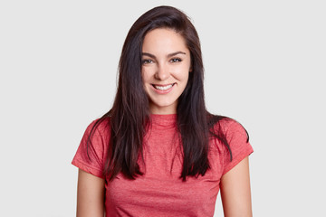 Beautiful brunette woman with pleasant smile, dark hair, dressed in casual pink t shirt, has white...