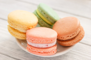 Fototapeta na wymiar Macaroons closeup on plate. Four colorful macaroon cookies on white wooden background