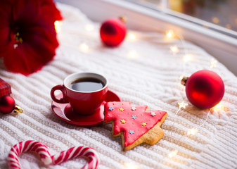 Red cup with espresso coffee and gingerbread in form of fir on white knitted plaid surrounded with winter decor.