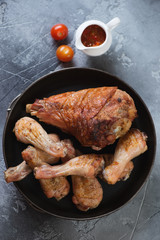Metal tray with barbecued turkey and chicken legs, flatlay on a grey stone background, vertical shot
