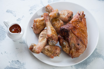 White plate with roasted turkey leg and chicken drumsticks, studio shot on a white concrete surface