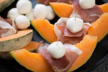 Cantaloupe melon slices with prosciutto and mozzarella balls, selective focus, closeup