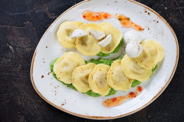 Plate of italian ravioli on a bedding of green peas puree, flatlay on a dark brown stone background, horizontal shot
