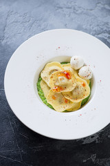 White plate with ravioli on a bedding of green peas puree, grey concrete background, vertical shot