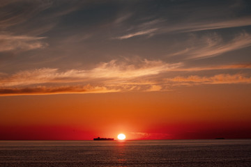 Silhouette of a container ship passing by on the horizon at sunset orange light. Skagen, Grenen in North Jutland in Denmark, Skagerrak, North Sea, Baltic Sea