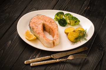 Steamed salmon, rise and broccoli on a white plate with knife and fork on a wooden table