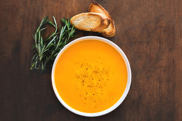 Pumpkin and carrot  Cream soup on rustic wooden table. Autumn Pumpkin cream-soup with rosemary herb and croutons. Top view. Copy space.