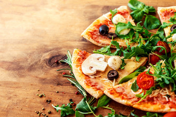 Hot pizza slice with Pepperoni, tomatoes, melting cheese on a rustic wooden table close up. Copy...