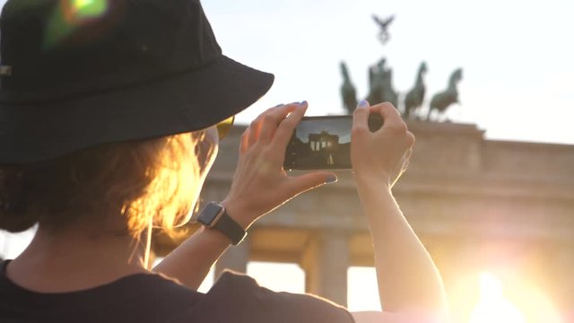 Traveler Tourist Woman Taking Photo Of Brandenburg Gate With Smartphone At Sunset