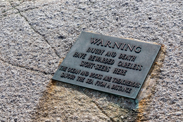 Closeup warning plaque on rocks at Peggy's Cove.