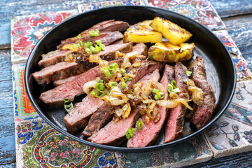 Barbecue dry aged wagyu flank steak with pineapples and onion rings as closeup on a plate