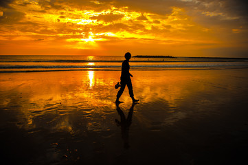 A person walks across a shimmering beach at sunset.